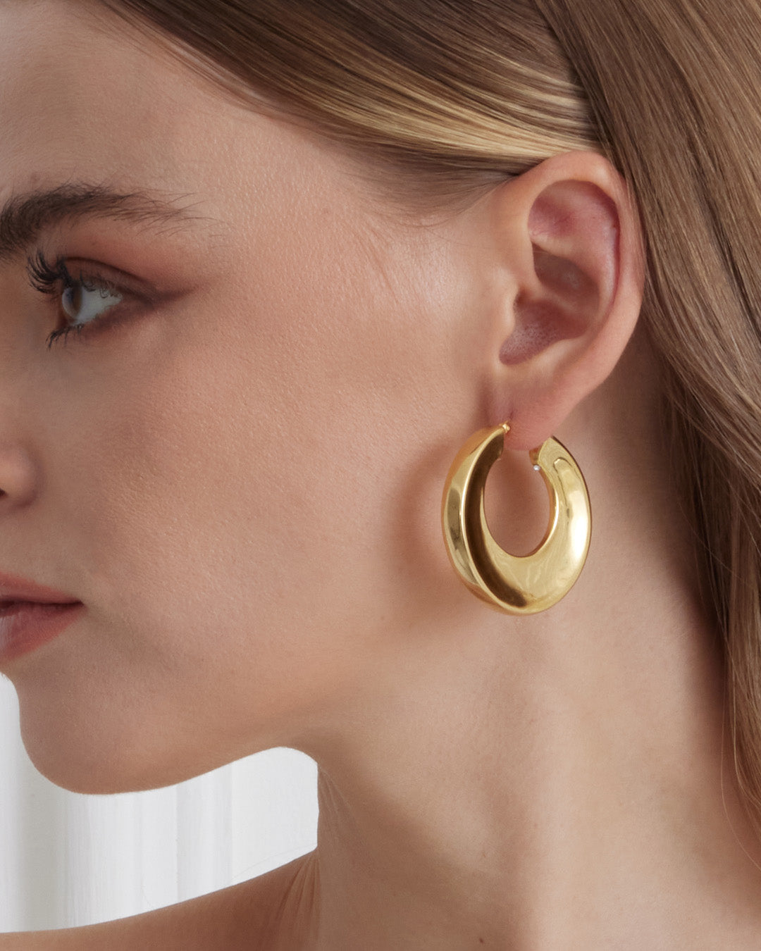 This is product picture of a large round shape organic hoop earrings with a slightly chunky look plated in gold in sterling silver material