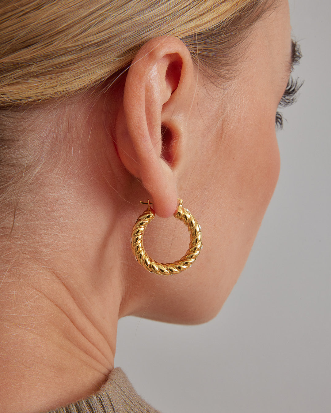 This is a product picture of a classical twisted rope pattern design with accented crystal set around the hoops earrings plated in gold in sterling silver material