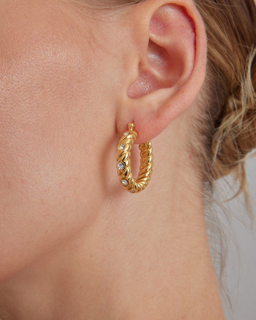 This is a product picture of a classical twisted rope pattern design with accented crystal set around the hoops earrings plated in gold in sterling silver material