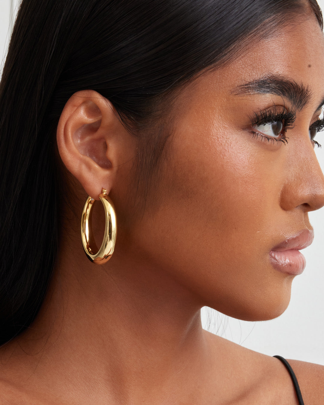 This is a product picture of chunky elongated oval shape hoop earring plated in gold in sterling silver material