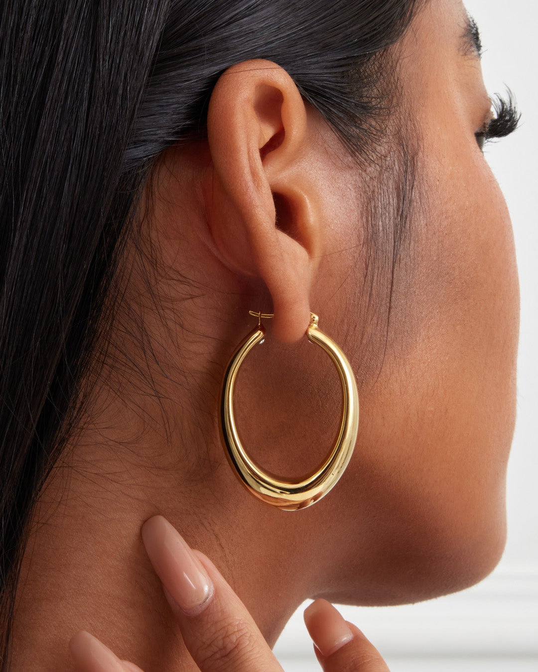 This is a product picture of chunky elongated oval shape hoop earring plated in gold in sterling silver material