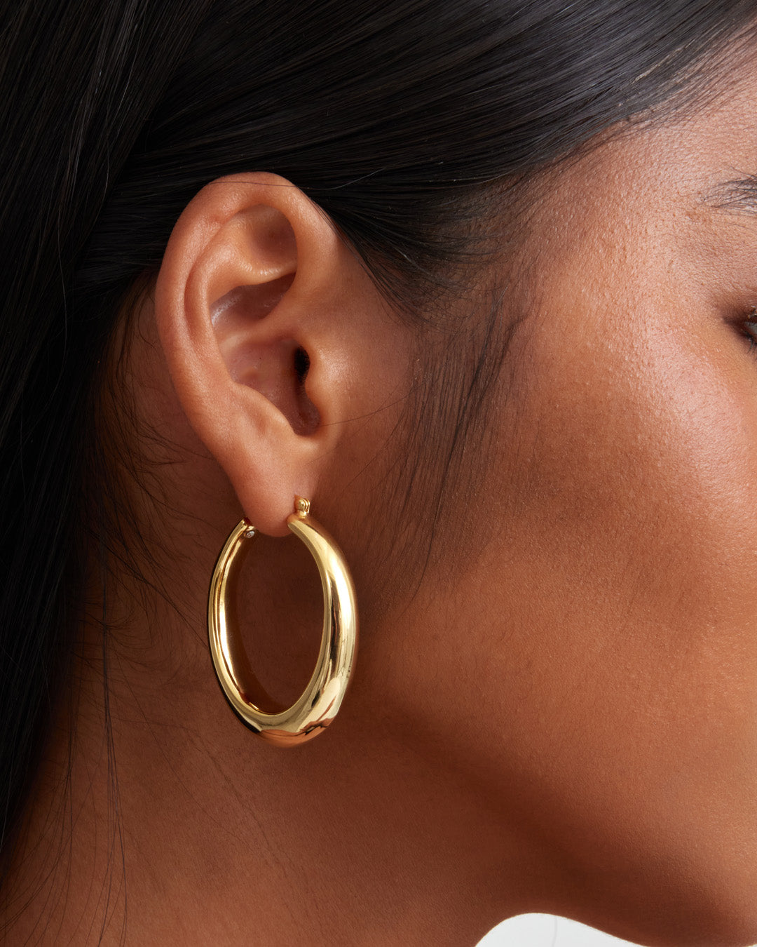 This is a product picture of chunky elongated oval shape hoop earring plated in gold in sterling silver material