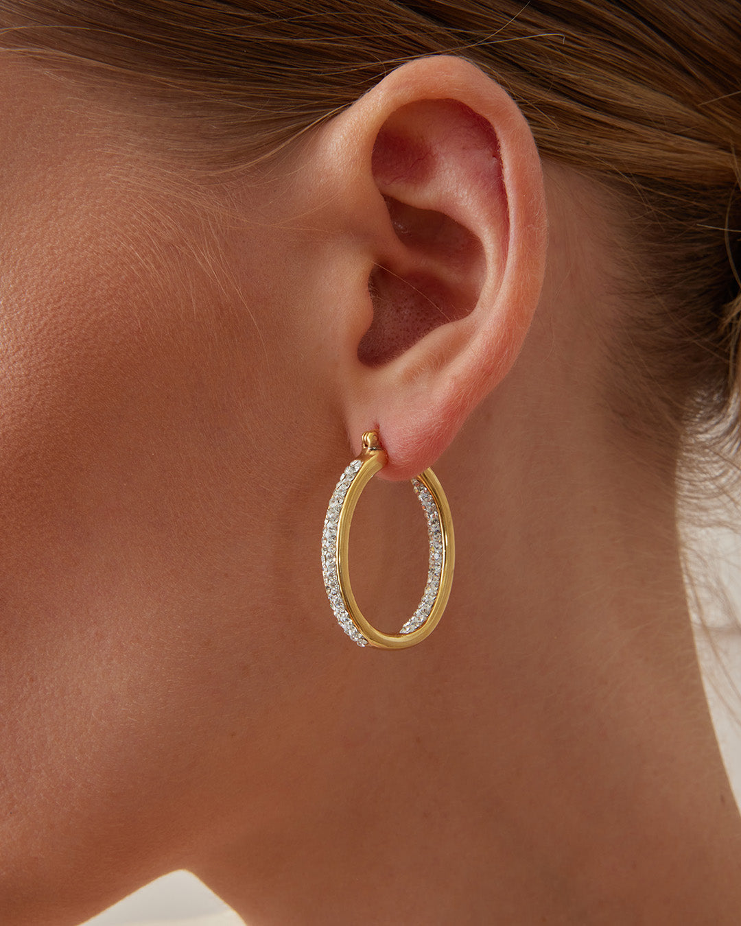 This is the product picture of elegant oval shape hoop earrings with micro pavé crystals plated in gold in sterling silver material