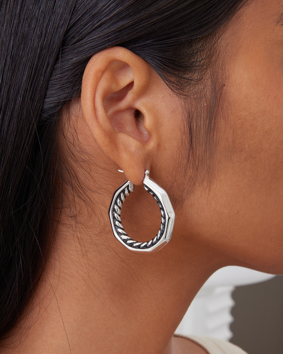 This is the product picture of a decagon shaped hoop earrings with a twisted rope design pattern plated in white gold in sterling silver material