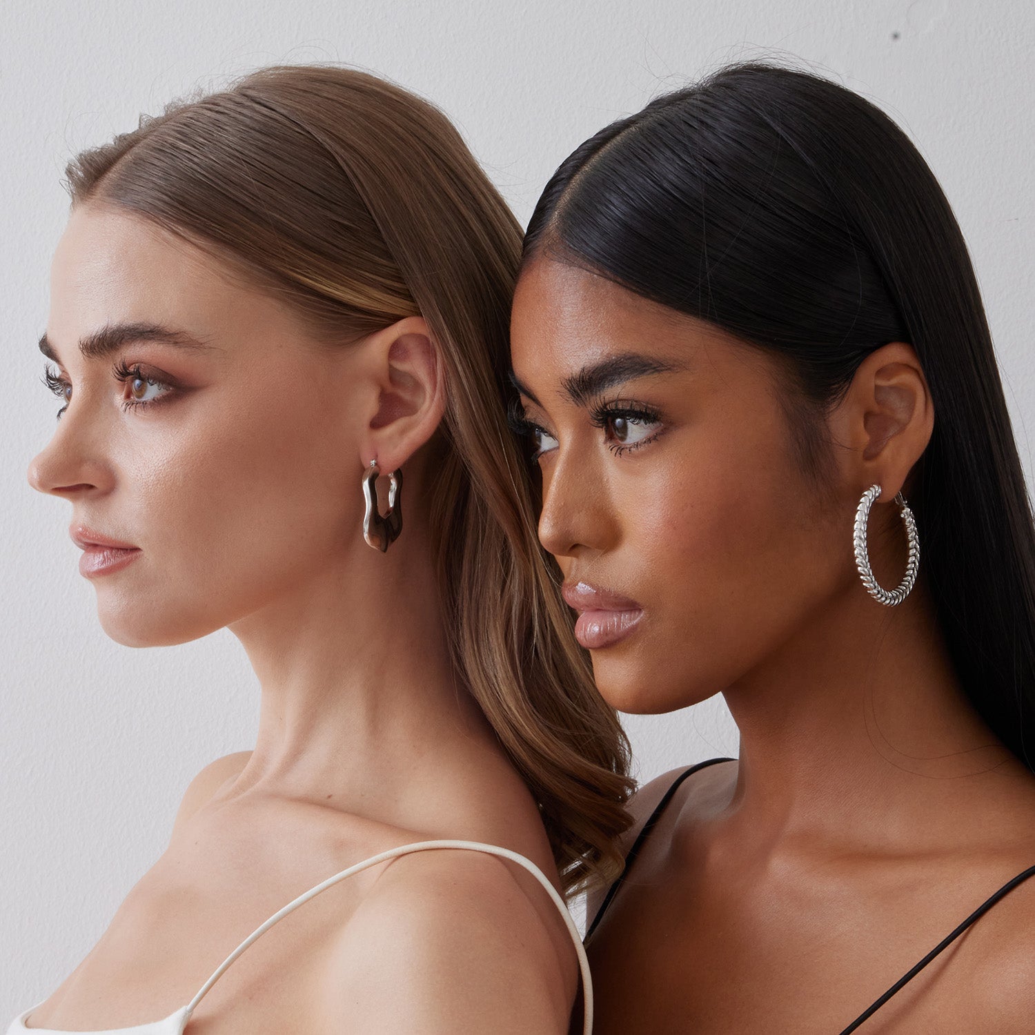 2 models wearing sterling silver hoop earrings plated with white gold